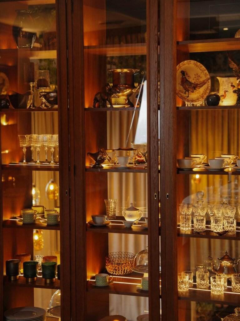 A sophisticated showcase of fine china, glassware, and home decor in a beautifully lit wooden cabinet.